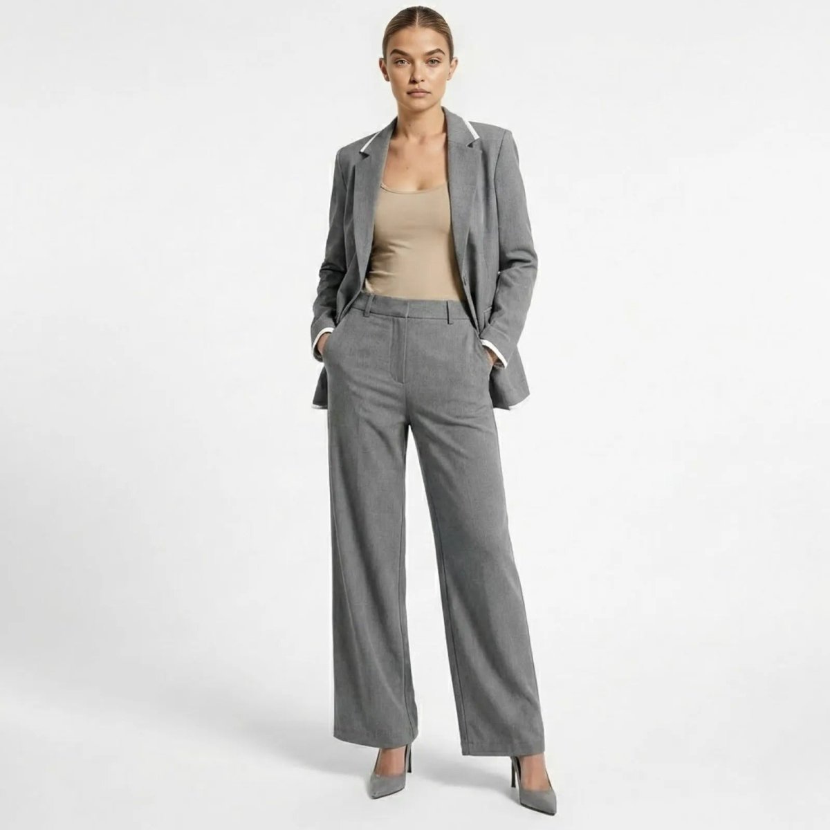Model facing forward wearing the Kouvr Lucia Set grey wide-leg pantsuit, featuring a relaxed blazer with white piping and matching high-waisted trousers.