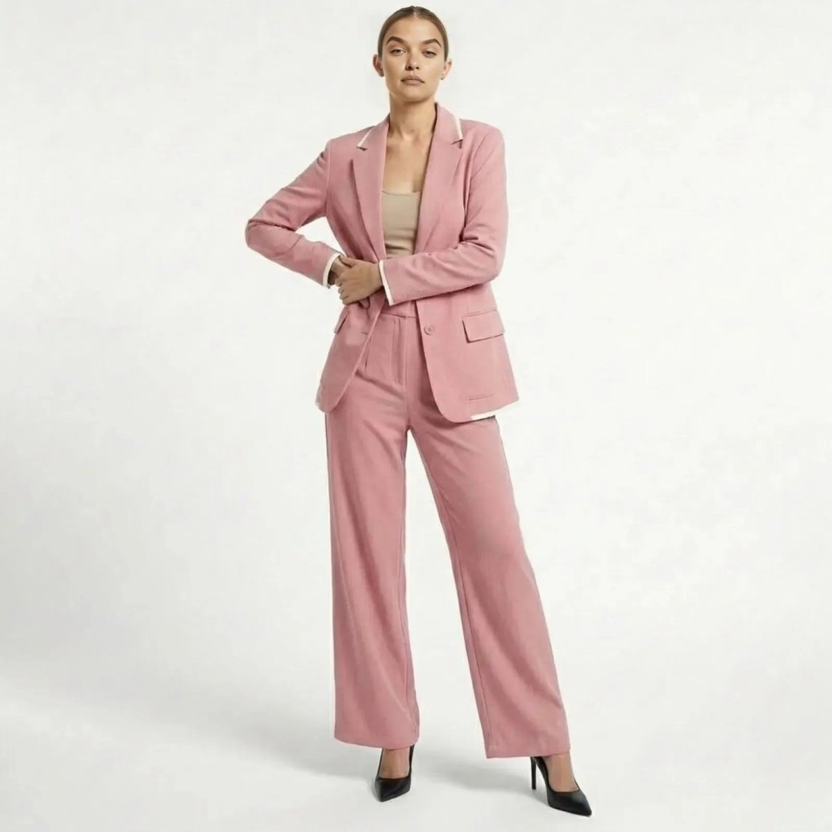A female model wearing the Kouvr Lucia Set  women's pink pantsuit with wide-leg trousers and a single-breasted blazer, posing confidently against a white background.