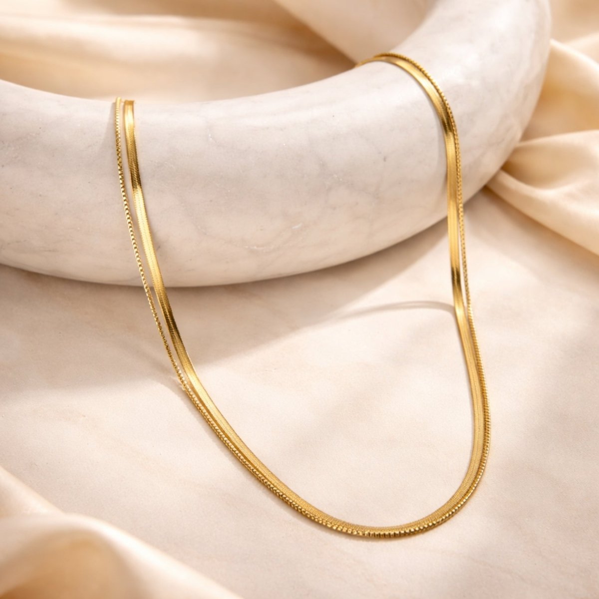 Kouvr double strand gold necklace set displayed elegantly on a white marble surface with silk fabric.