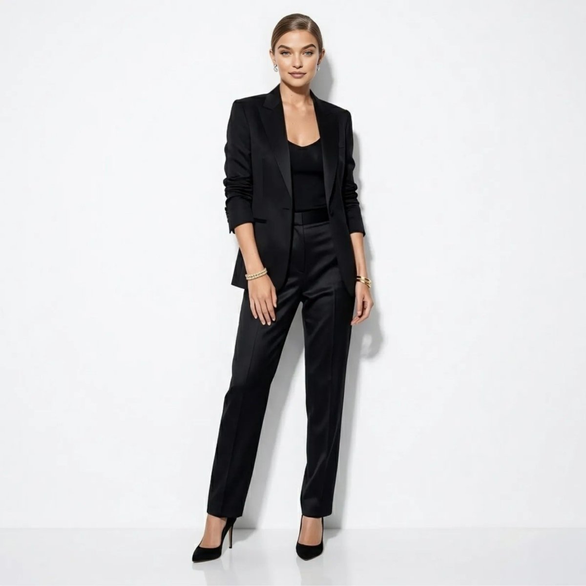 A woman in a stylish black pantsuit accessorizing with the Kouvr Marzanna double row gold bracelet on each wrist.
