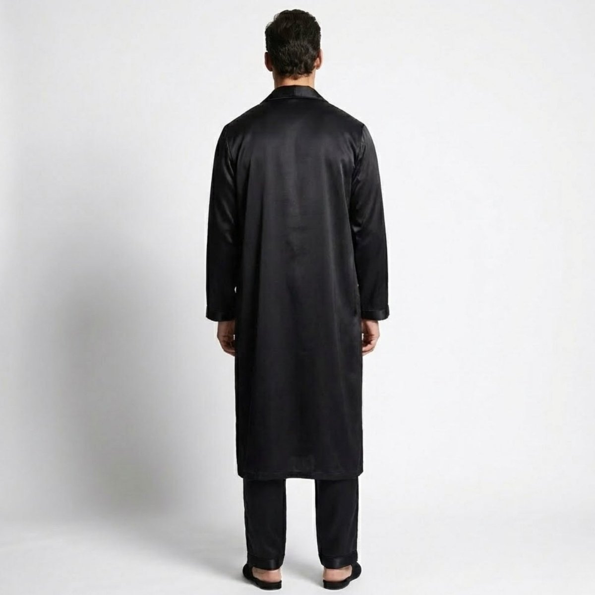 Back view of a man wearing a Kouvr long black silk robe over matching pajama pants.