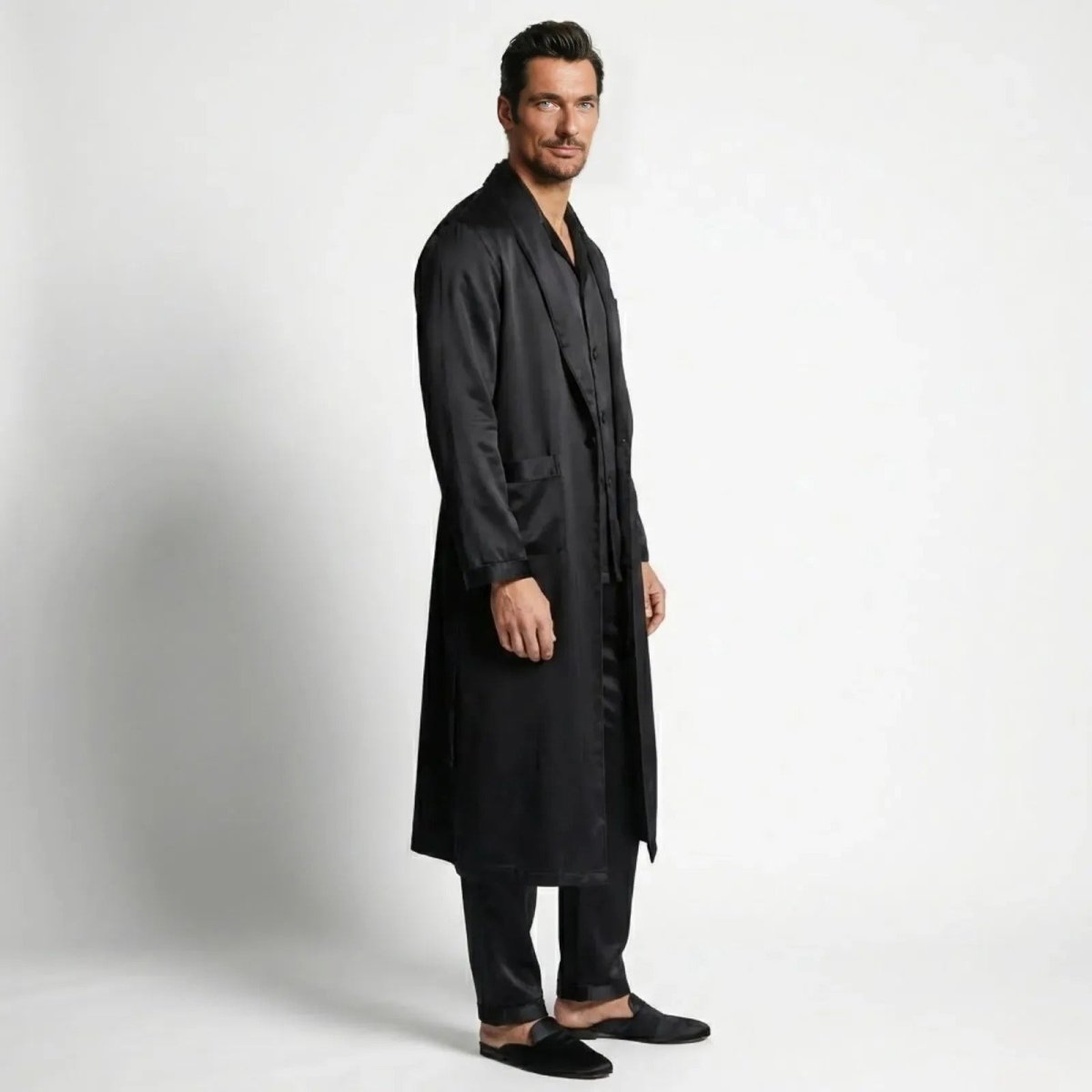 Man in a Kouvr black silk pajama set and matching long robe, shown from the side to display the garment's drape.