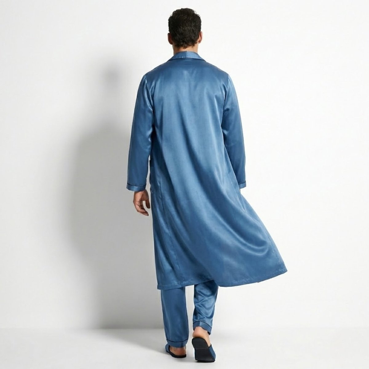 Back view of a man wearing a Kouvr azure blue long satin robe over matching pajama pants.