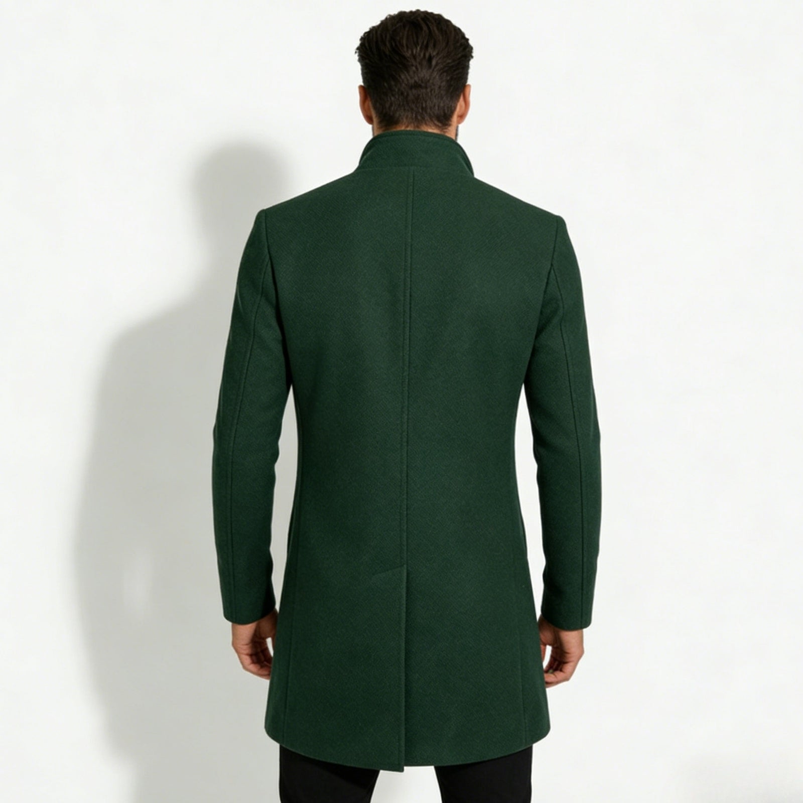Back view of a man wearing a Kouvr dark green winter overcoat, highlighting the center vent and structured shoulders.