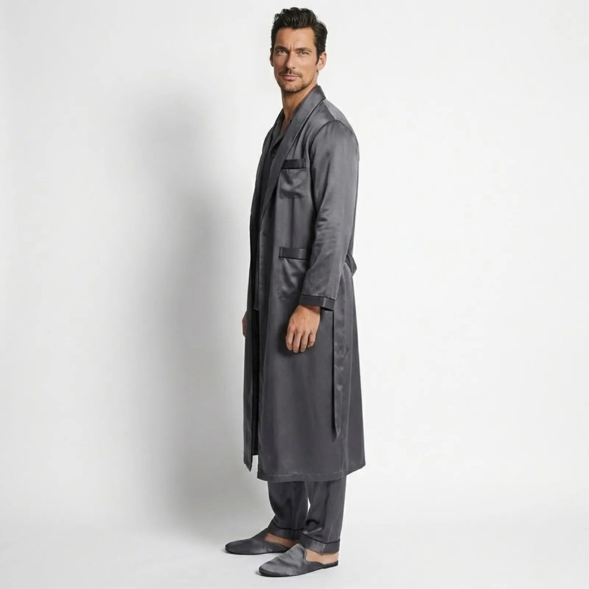Side profile of a male model in the Kouvr darkl grey satin robe and pajama set, showing the drape of the fabric and the belted waist. 