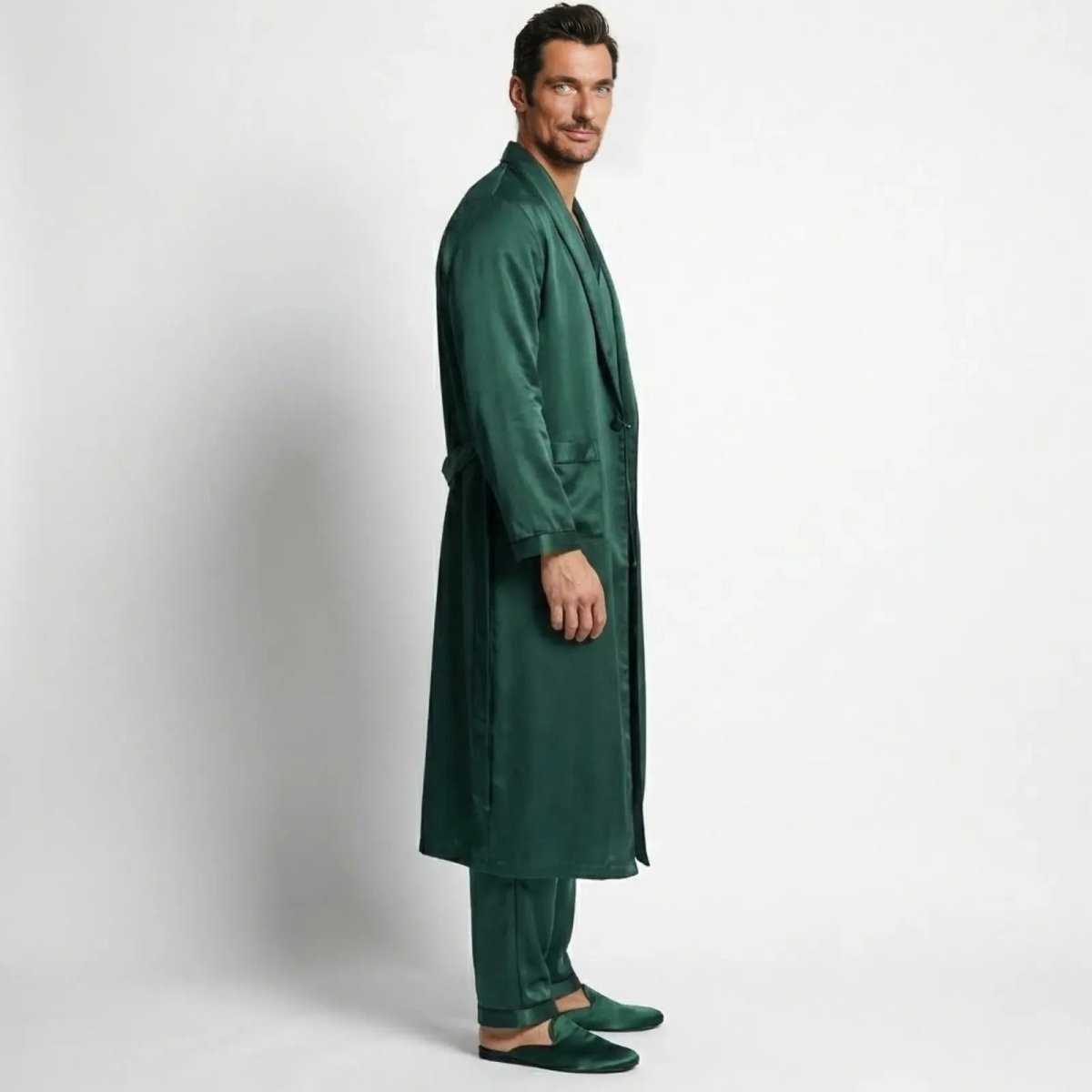 Side profile of a male model in a green satin long robe and matching pajama pants, showing the drape and length of the luxury loungewear set.
