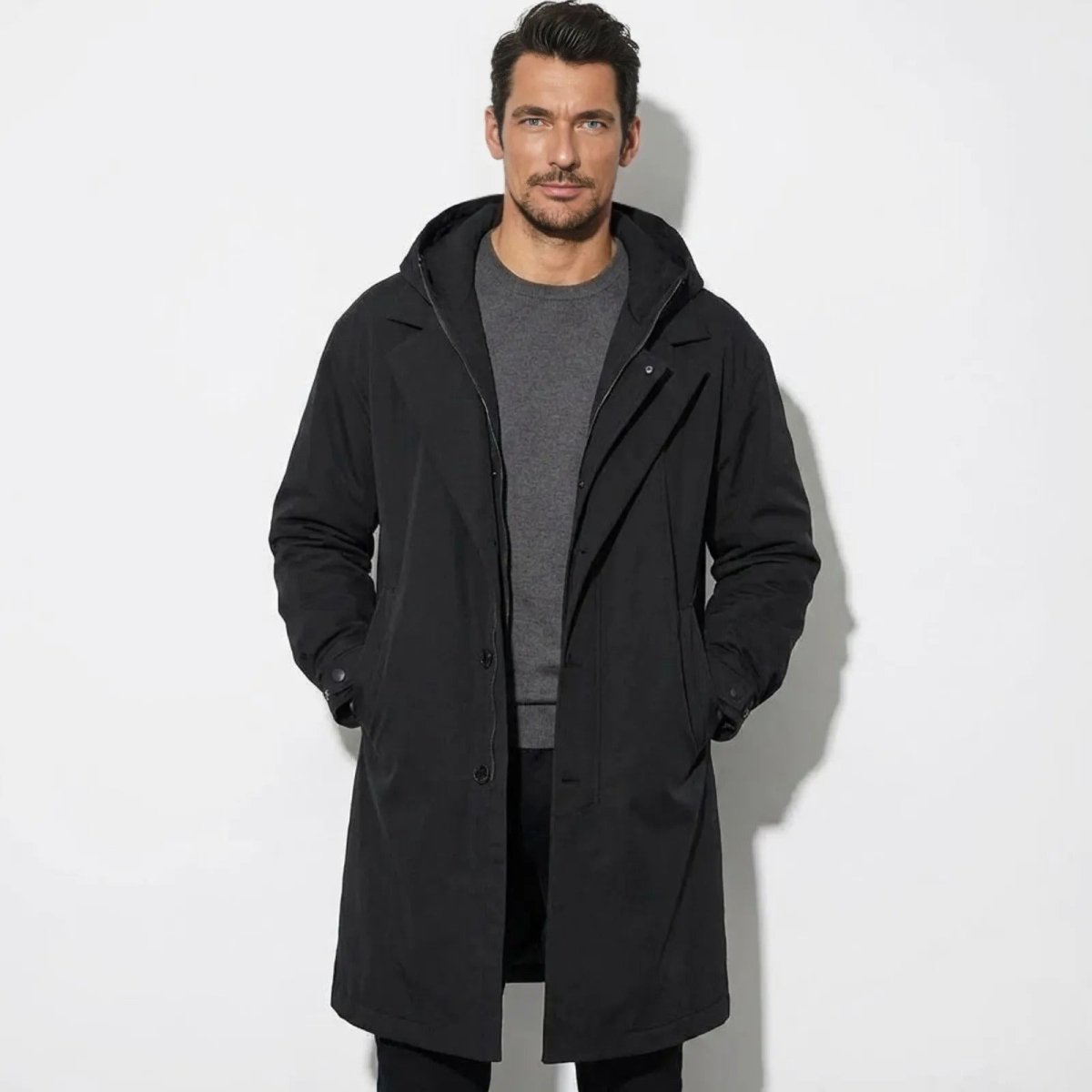 Man wearing the black Kouvr hooded technical coat with a grey sweater, viewed from the front.