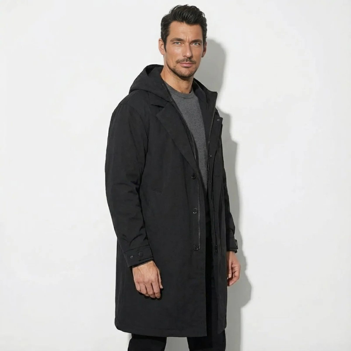 Side angle view of a man in a black knee-length Kouvr technical parka, showing its silhouette and fit.