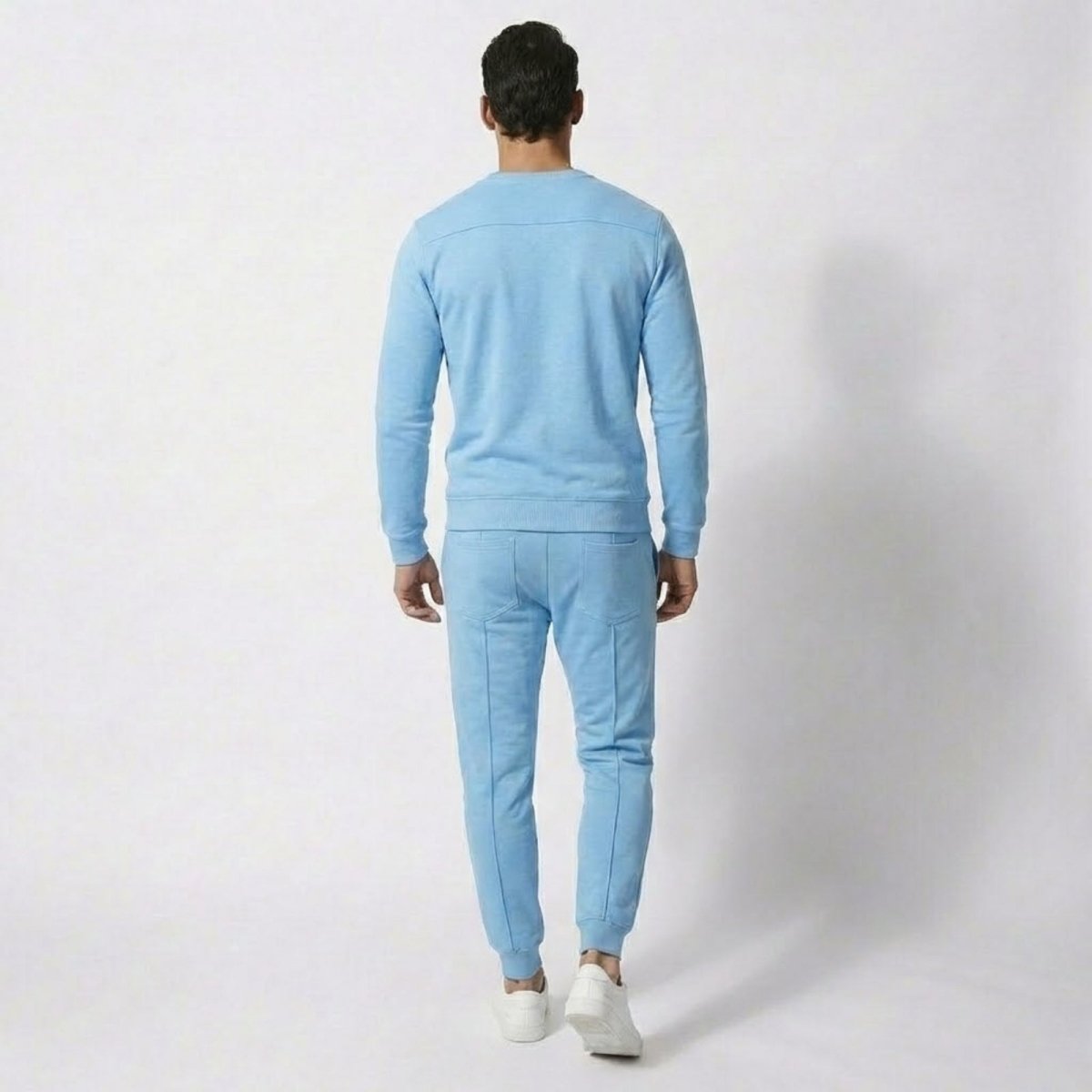 Rear view of a male model wearing the Kouvr light blue crewneck sweatshirt and matching tapered joggers, showing back pocket details.