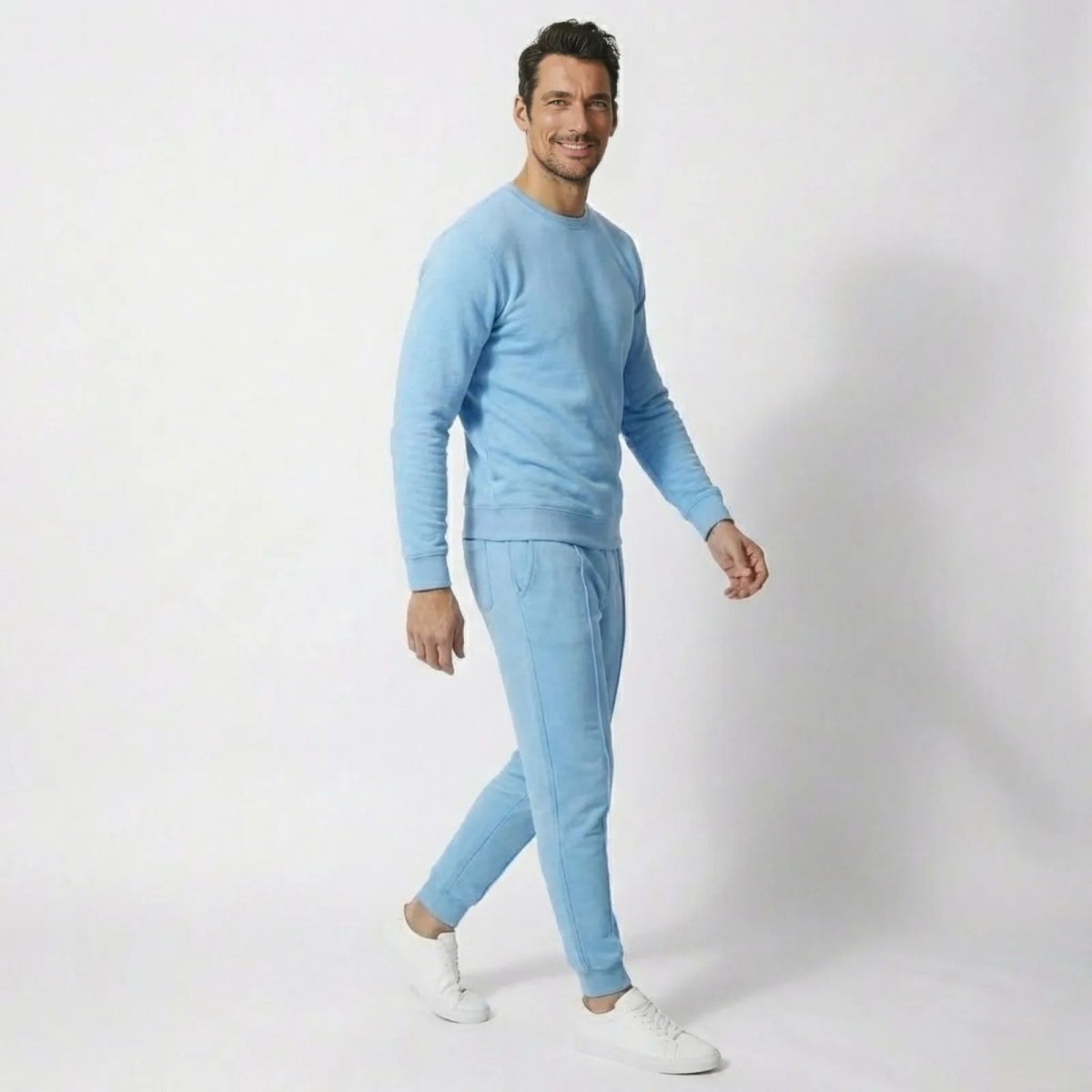 Male model in a side profile view walking while wearing the Kouvr sky blue sweatsuit with white sneakers.