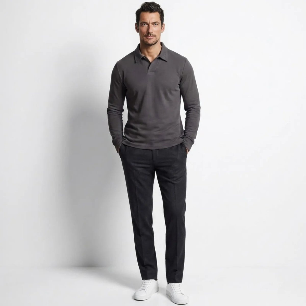 Man wearing the Kouvr Rome Long Sleeve Polo in charcoal grey, styled with dark trousers and white sneakers, shown from the front.