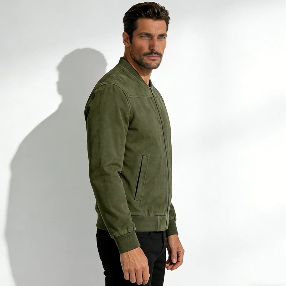 Side profile of a man in a Kouvr handcrafted olive suede bomber jacket showing its tailored fit.
