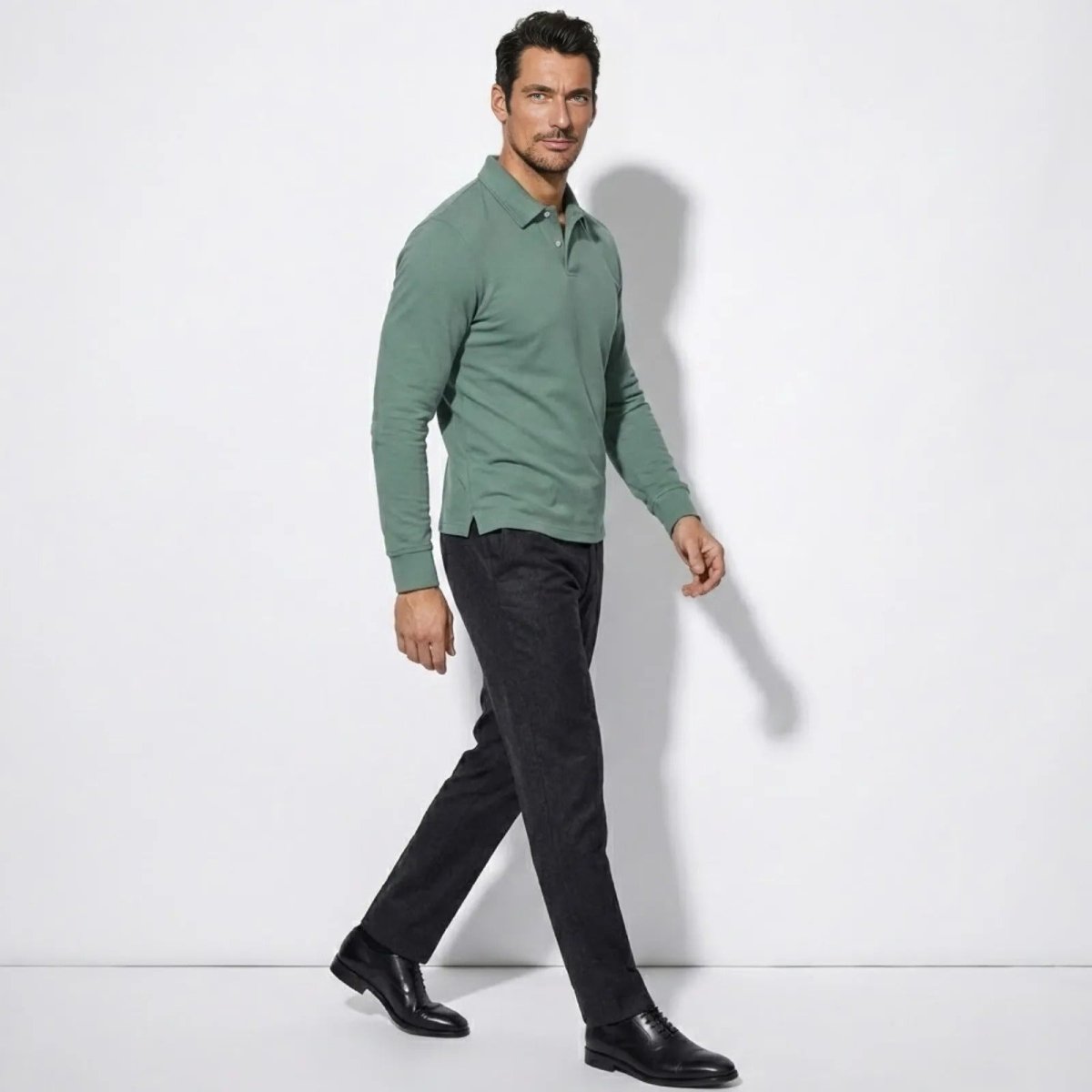 Model in a side profile walking pose wearing the Kouvr slim fit long sleeve polo in sage green to show the garment's drape and fit.