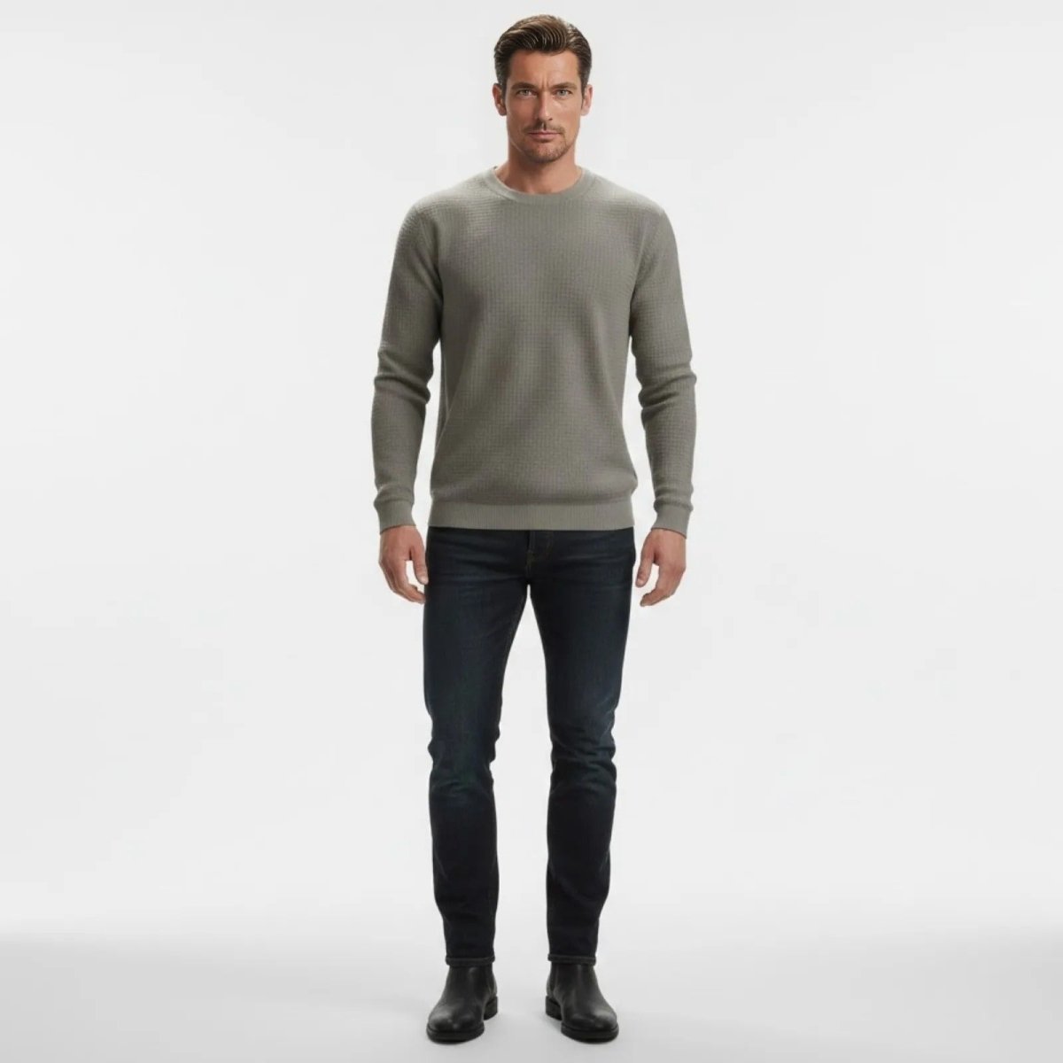 Male model facing forward wearing the Kouvr grey waffle knit crewneck sweater paired with slim-fit dark wash jeans and black boots on a white background.