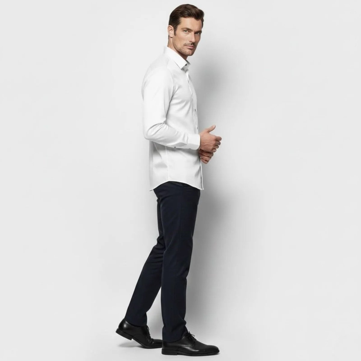 Side profile of a male model walking in the Kouvr Fashion white performance-stretch dress shirt and dark trousers to show the slim fit silhouette.