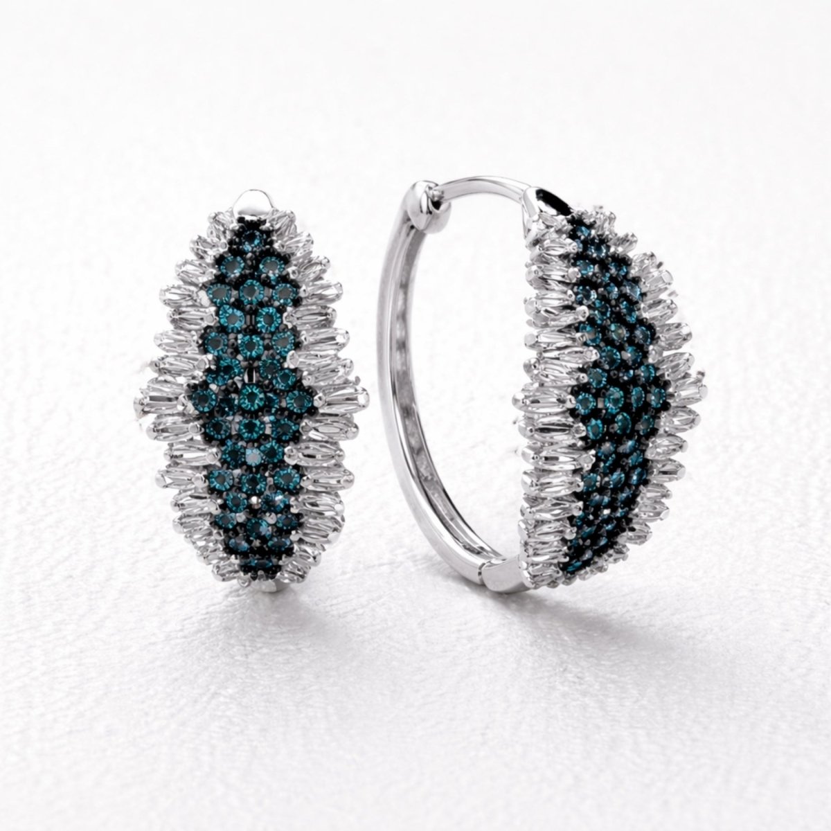 A pair of Kouvr Midnight Lark sapphire and diamond huggie hoop earrings with a central band of blue sapphires and outer bands of pave diamonds in 18k white gold, displayed in a dark velvet jewelry box.