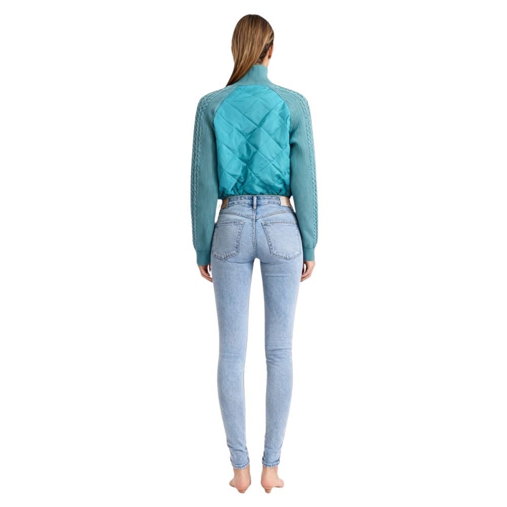 Model wearing the Kouvr Mika Hybrid Bomber Jacket in Aegean Teal, featuring cable-knit sleeves and a diamond-quilted body, paired with light-wash skinny jeans and white sneakers