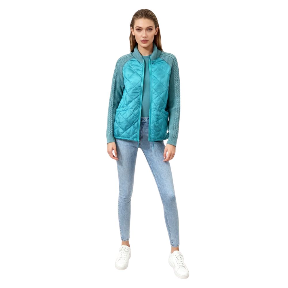 Model wearing the Kouvr Mika Hybrid Bomber Jacket in Aegean Teal, featuring cable-knit sleeves and a diamond-quilted body, paired with light-wash skinny jeans and white sneakers