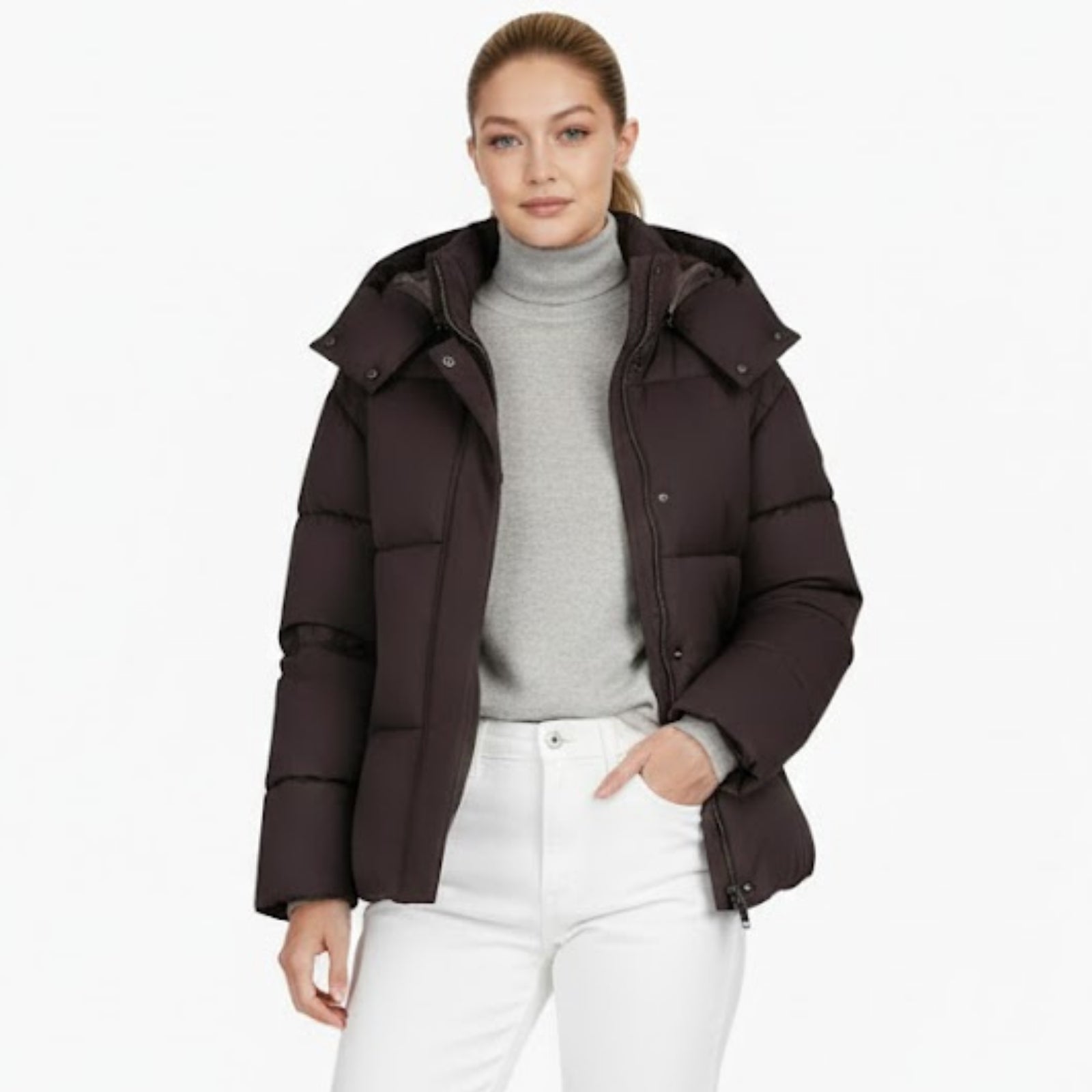 Woman wearing the Kouvr Miranda hooded puffer jacket in espresso brown, styled with a grey turtleneck sweater and white denim pants.