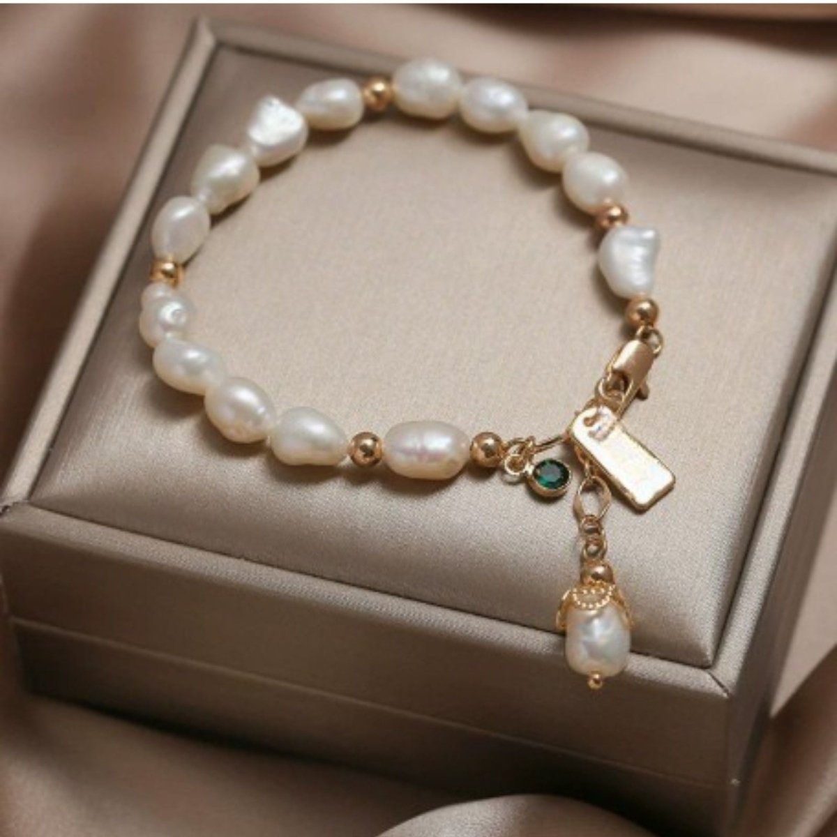 The Nathalia Baroque Pearl Bracelet by Kouvr Fashion with 18k gold beads, an emerald charm, and a pearl drop charm on a white background.