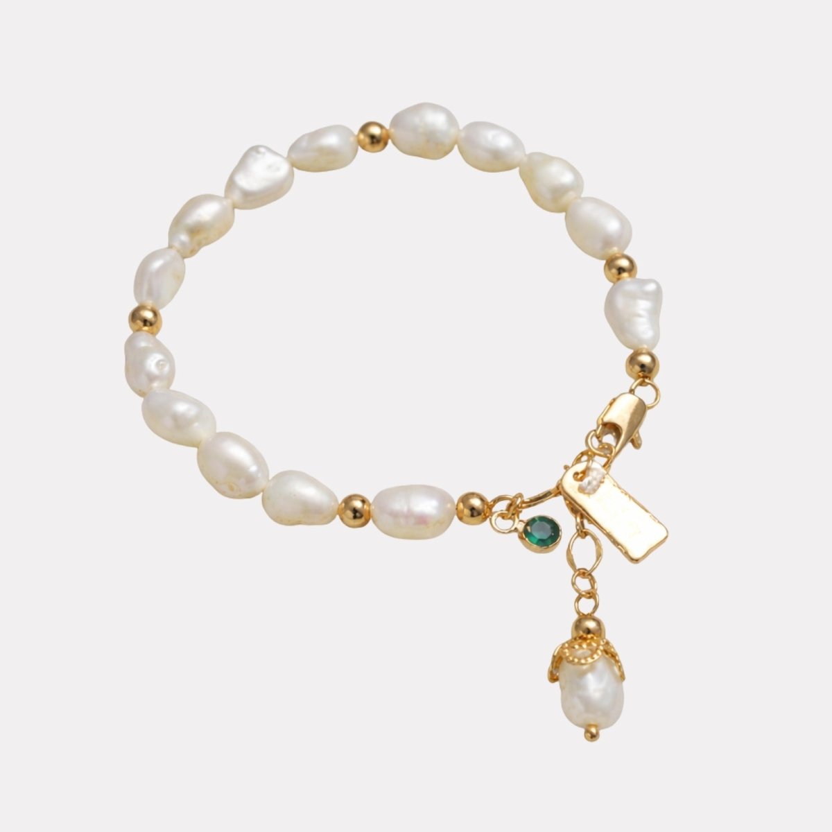The Nathalia Baroque Pearl Bracelet by Kouvr Fashion with 18k gold beads, an emerald charm, and a pearl drop charm on a white background.