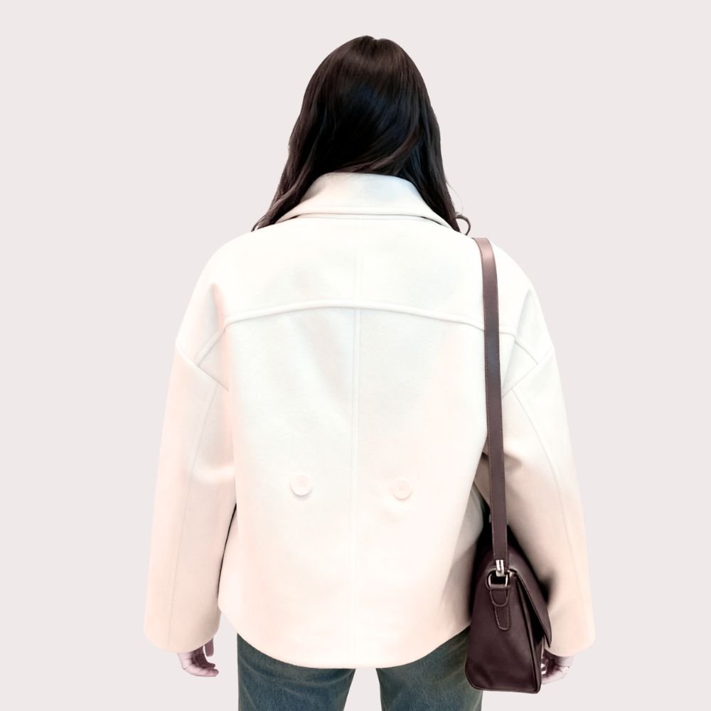 Model wearing the Niana short coat in ivory, styled with a white turtleneck and brown shoulder bag