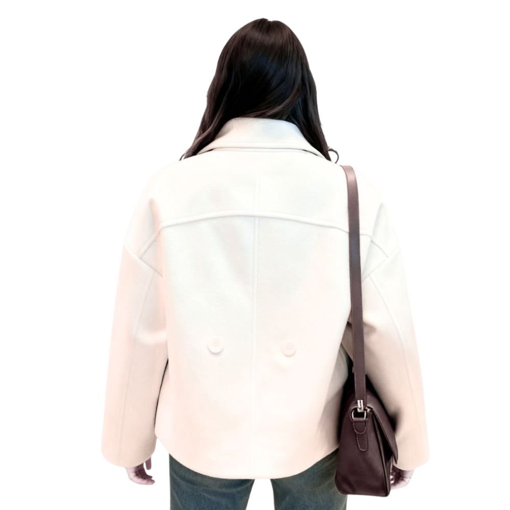 Model wearing the Niana short coat in ivory, styled with a white turtleneck and brown shoulder bag