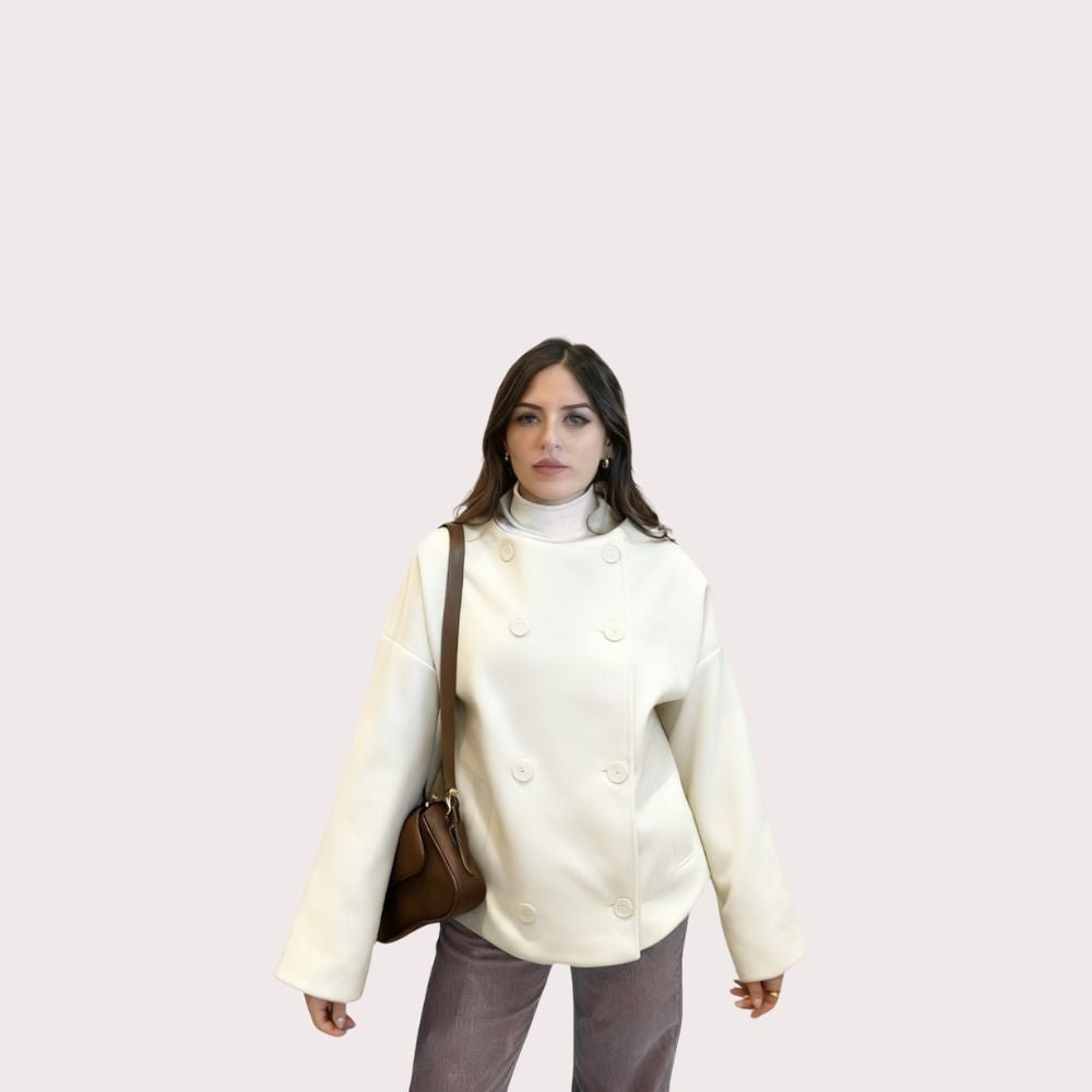 Model wearing the Niana short coat in ivory, styled with a white turtleneck and brown shoulder bag