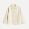Model wearing the Niana short coat in ivory, styled with a white turtleneck and brown shoulder bag