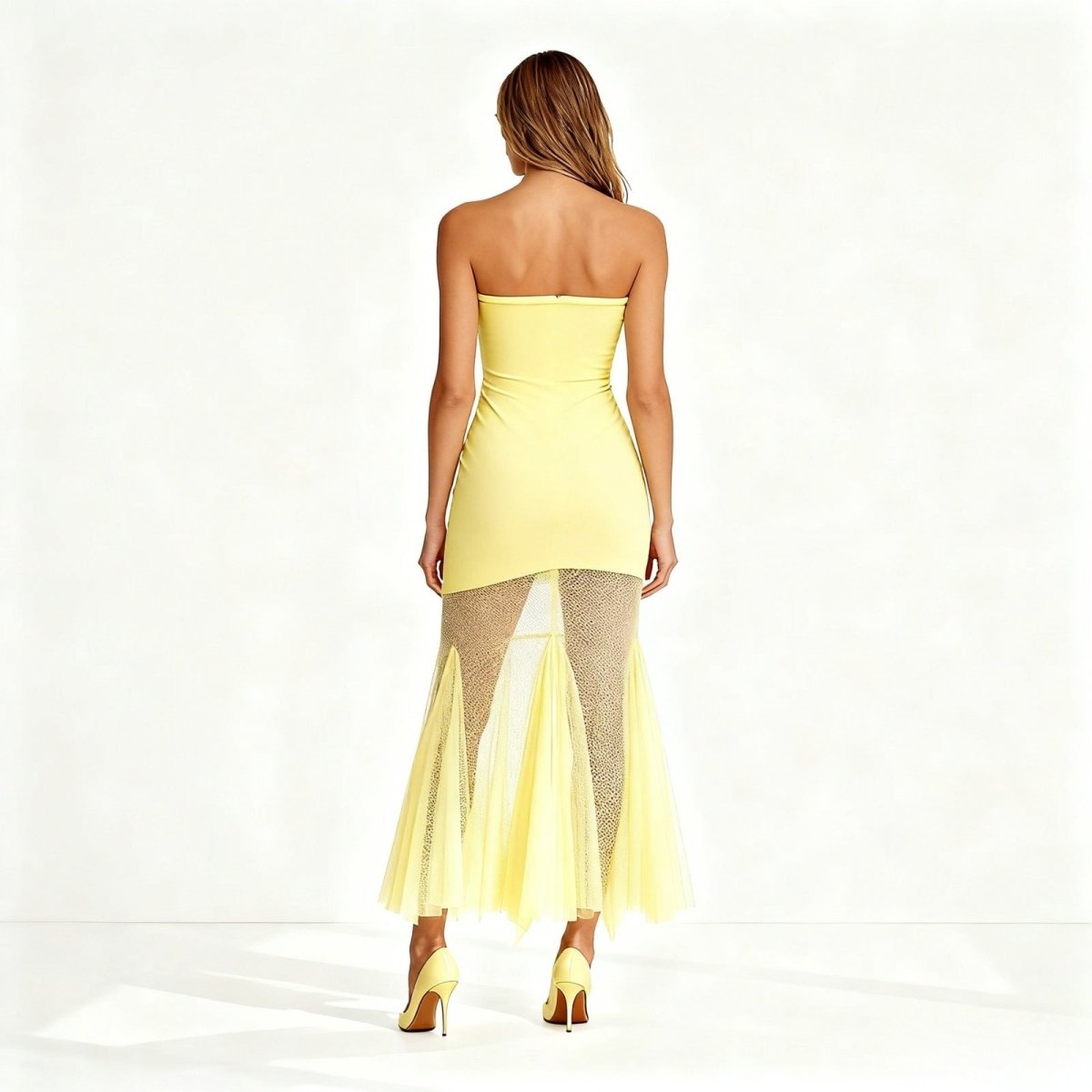 Woman wearing a strapless yellow dress with a sheer overlay on a white background