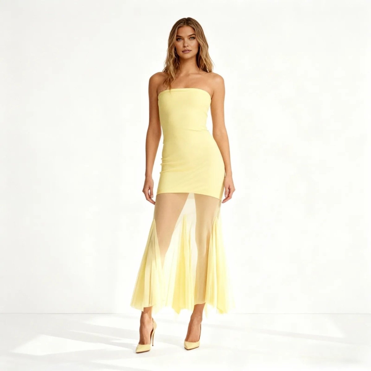 Woman wearing a strapless yellow dress with sheer overlay on a white background
