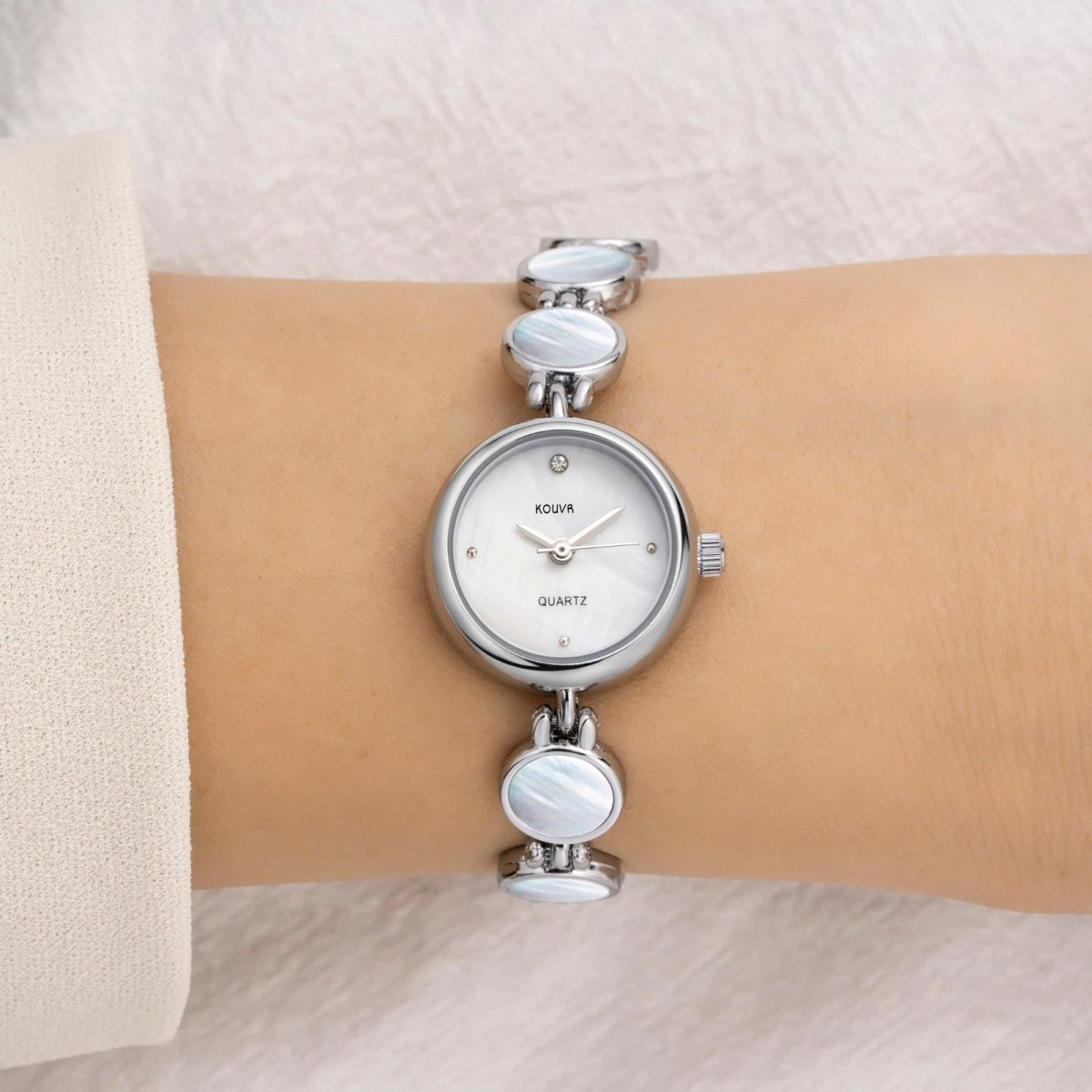 A woman wearing the Kouvr Pearl silver Faelan gold-tone watch with a white mother of pearl bracelet and dial.