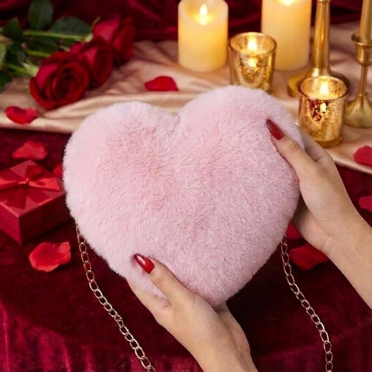 A woman with red nails holding a soft pink faux fur heart-shaped purse in front of a romantic candlelit setting with red roses.
