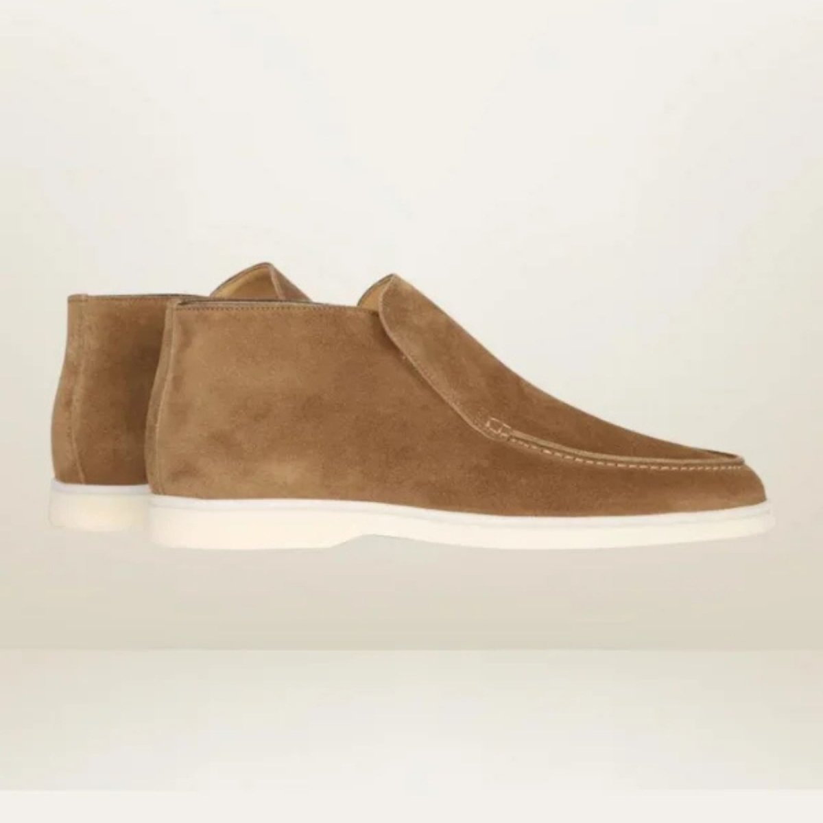 Kouvr suede ankle loafer boots with tan chino pants.
Side view of black Italian suede slip-on boots with a contrasting white sole, worn by a model. 