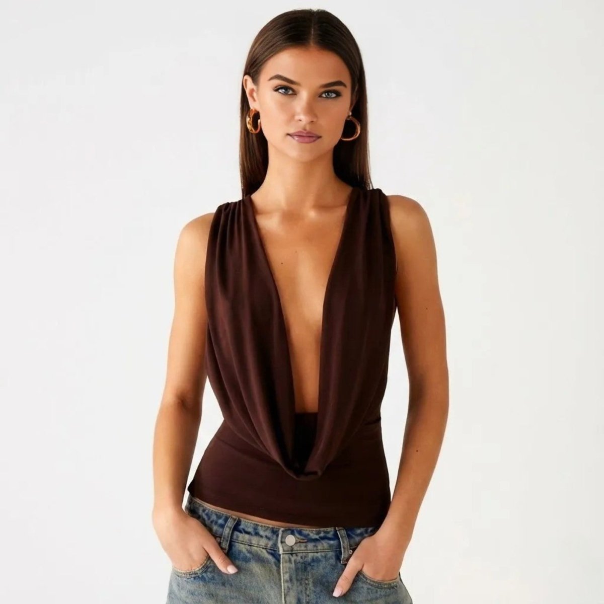 Model wearing the Rhea dark brown cowl neck top from Kouvr, featuring a deep plunging neckline and draped front, paired with jeans.