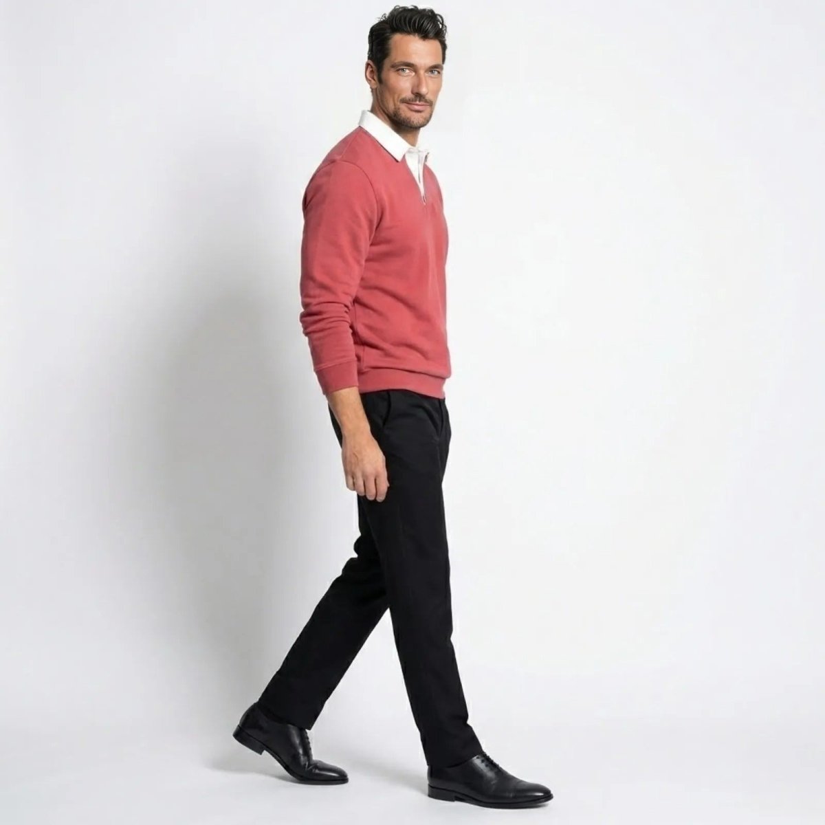 Side profile of a model walking in the Kouvr Rhodes rosewood red polo sweater and black trousers.