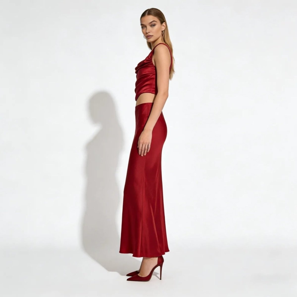 Side view of a model in a red satin cowl neck top and bias cut maxi skirt set, showing the elegant silhouette and drape of the fabric.