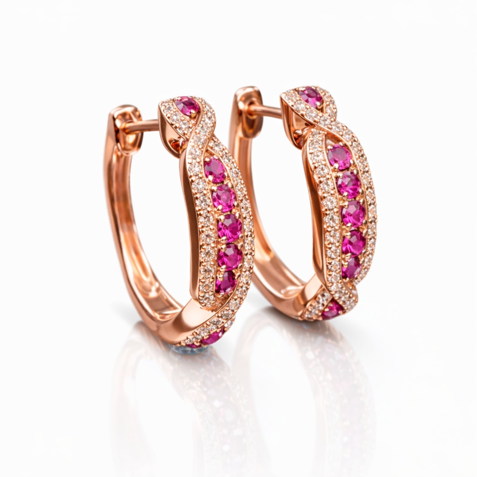 A pair of 18k rose gold infinity hoop earrings featuring a row of red rubies bordered by pave-set diamonds on a white reflective surface by Kouvr.