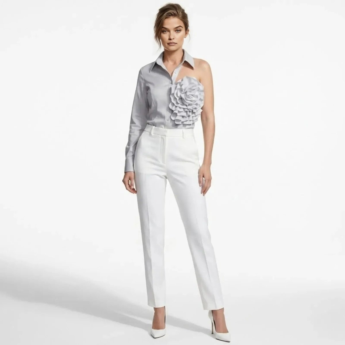 Model wearing the Kouvr grey one-shoulder shirt with a large floral rosette appliqué, paired with white tailored trousers.