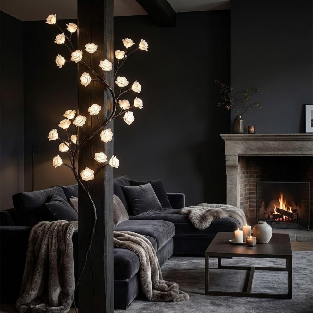 The Kouvr sculptural tree branch light fixture installed on a wooden beam next to a dark velvet sectional sofa and a lit stone fireplace.