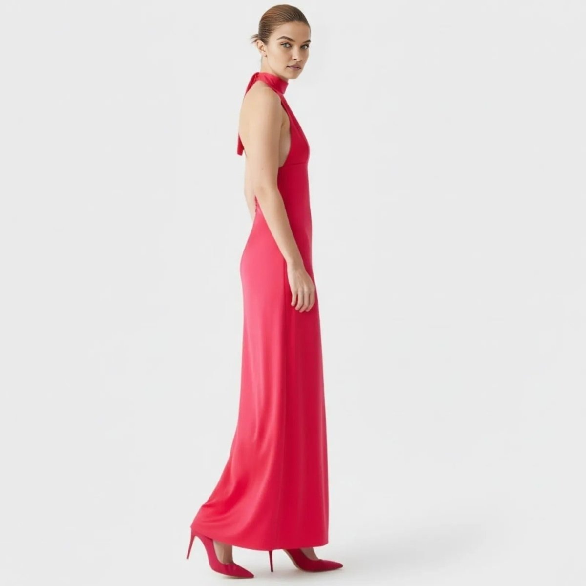  Side profile of a model in the Kouvr Sharon fuchsia red halter dress, showing the elegant silhouette and floor length design.