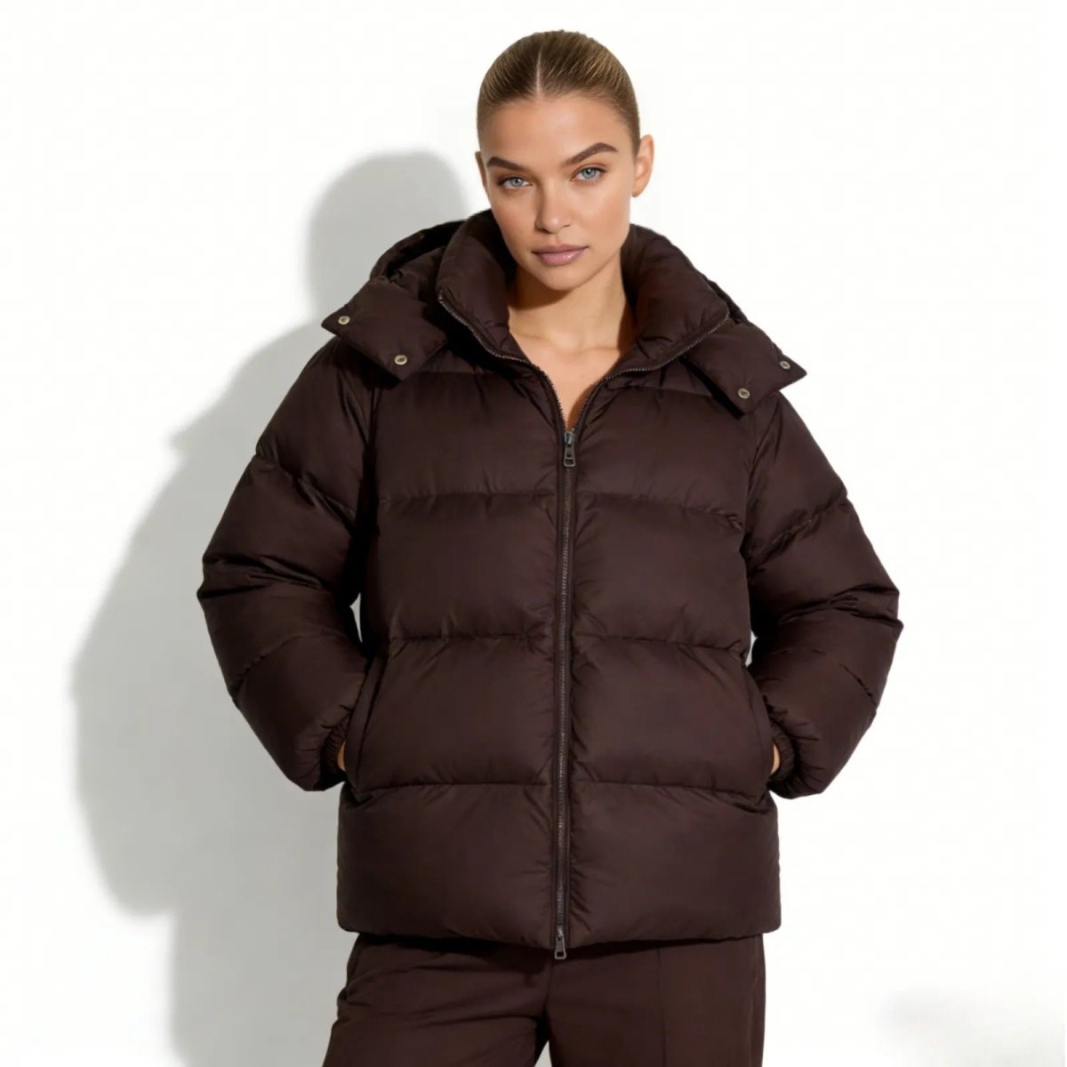 Model wearing the Kouvr Sheena hooded puffer jacket in a rich dark brown, zipped up with hands in pockets.