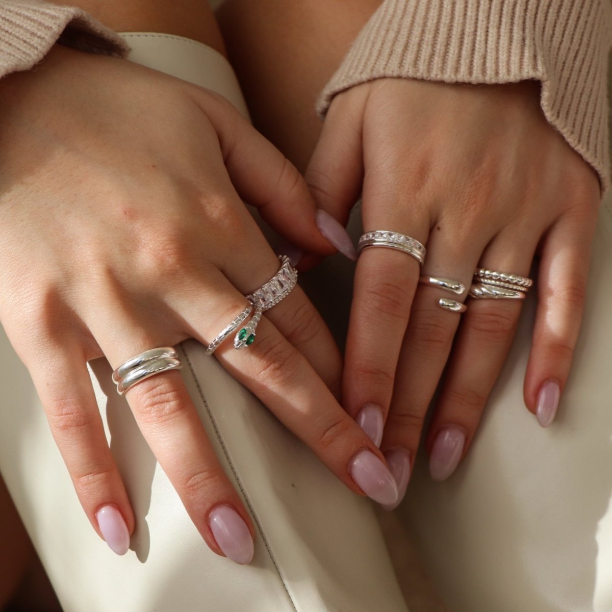 Close-up of hands with multiple silver rings on a neutral background