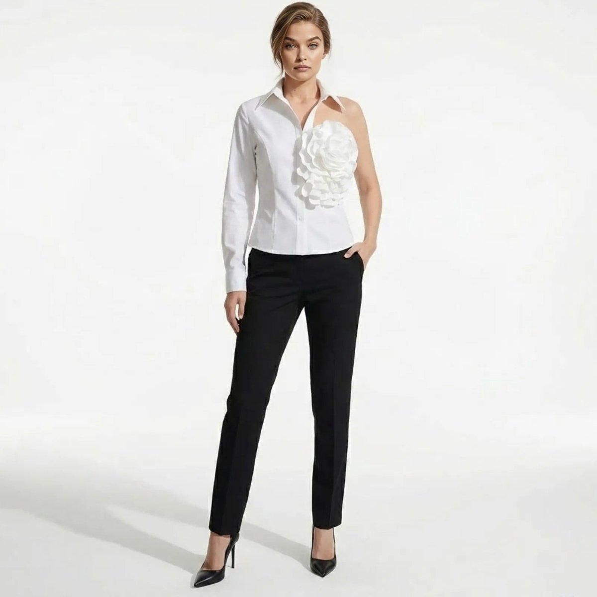 Model wearing the Kouvr Teresa one-shoulder white shirt with a large floral appliqué, paired with black tailored trousers, shown from the front.