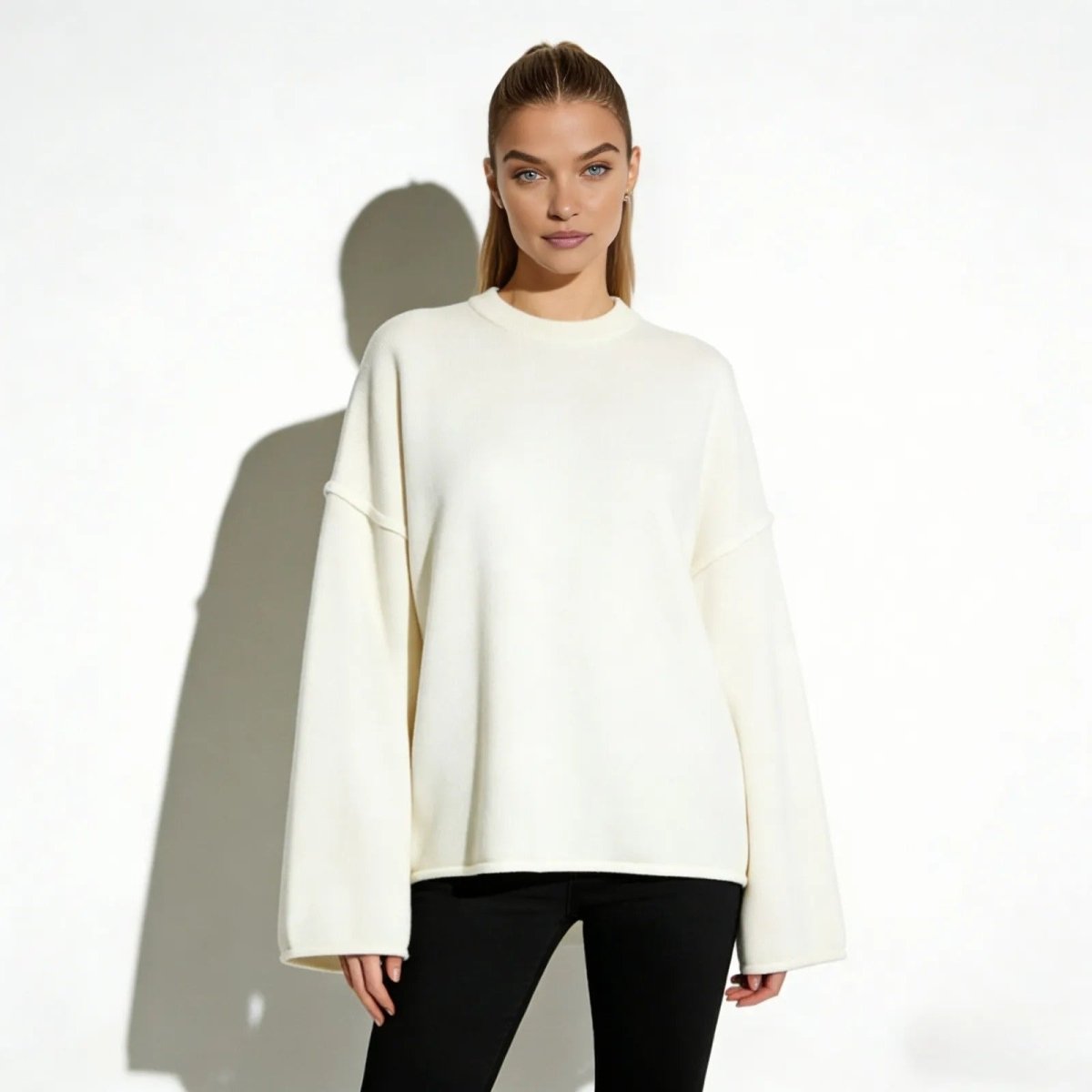Model wearing the Kouvr Krystal oversized cream sweater with a boxy fit and wide sleeves, styled with black pants against a white background.