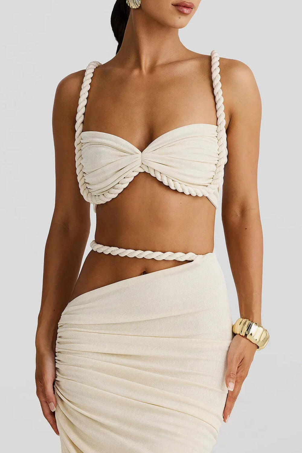 Model wearing Kouvr's The Thelma Set, a beige two-piece Grecian outfit featuring a rope detail bralette top and a ruched asymmetrical maxi skirt