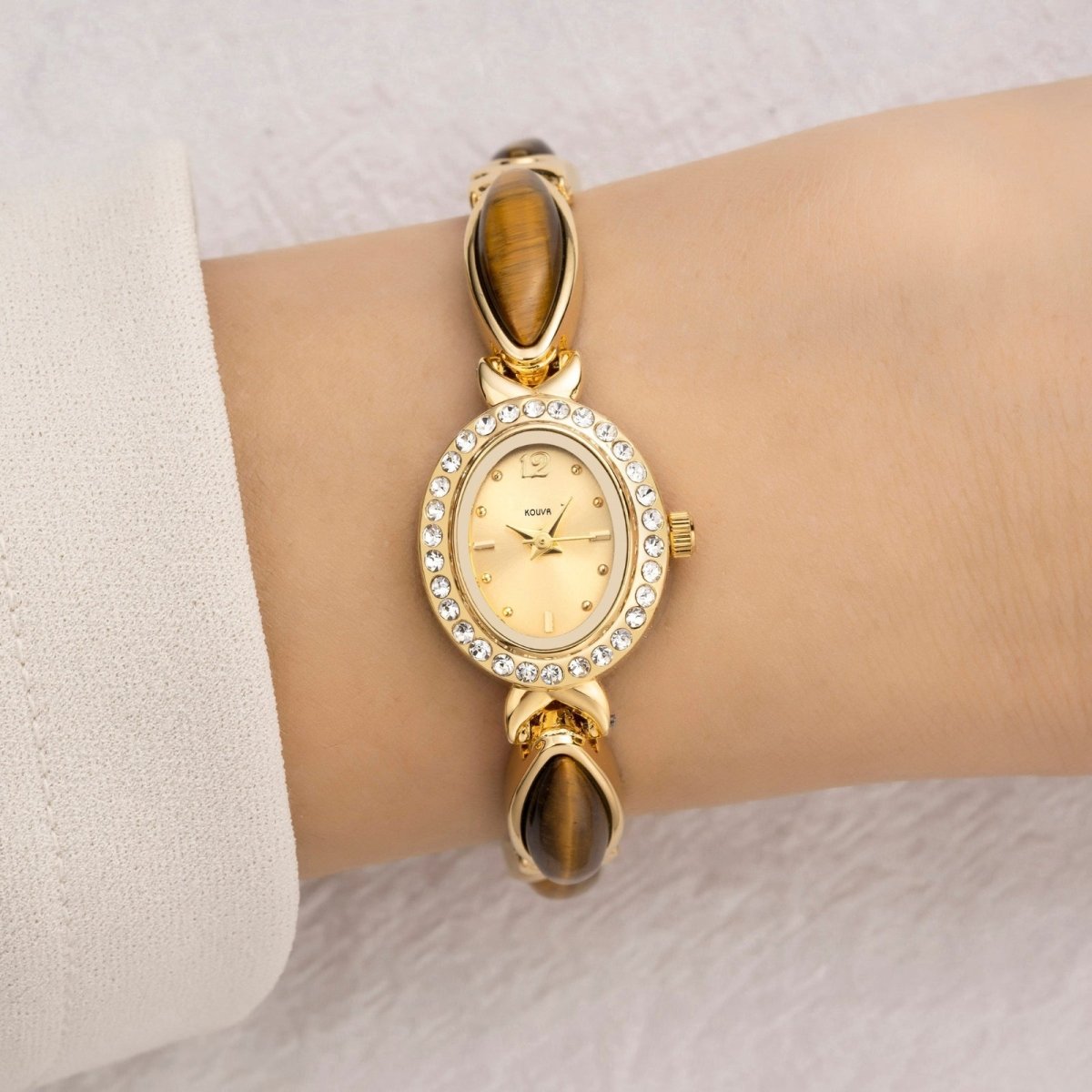 A woman wearing the elegant Kouvr Tiger's Eye and gold bracelet watch, paired with a white sleeve.