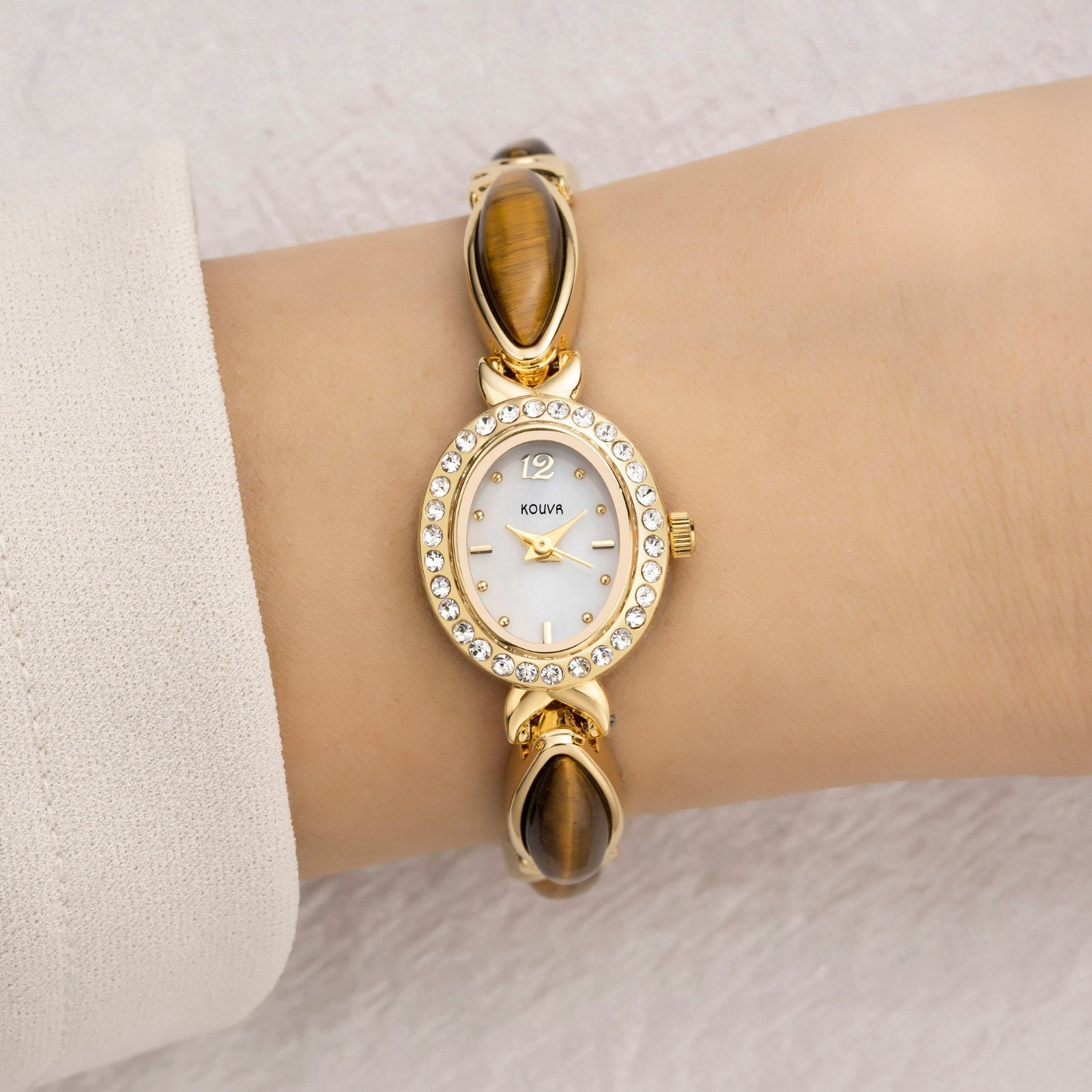 A woman wearing the elegant Kouvr Tiger's Eye and white gold bracelet watch, paired with a white sleeve