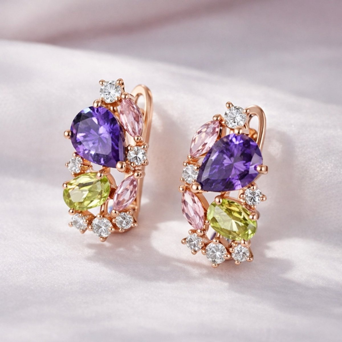 A pair of Kouvr Vanya colorful gemstone earrings in rose gold resting on a soft, folded white silk fabric.