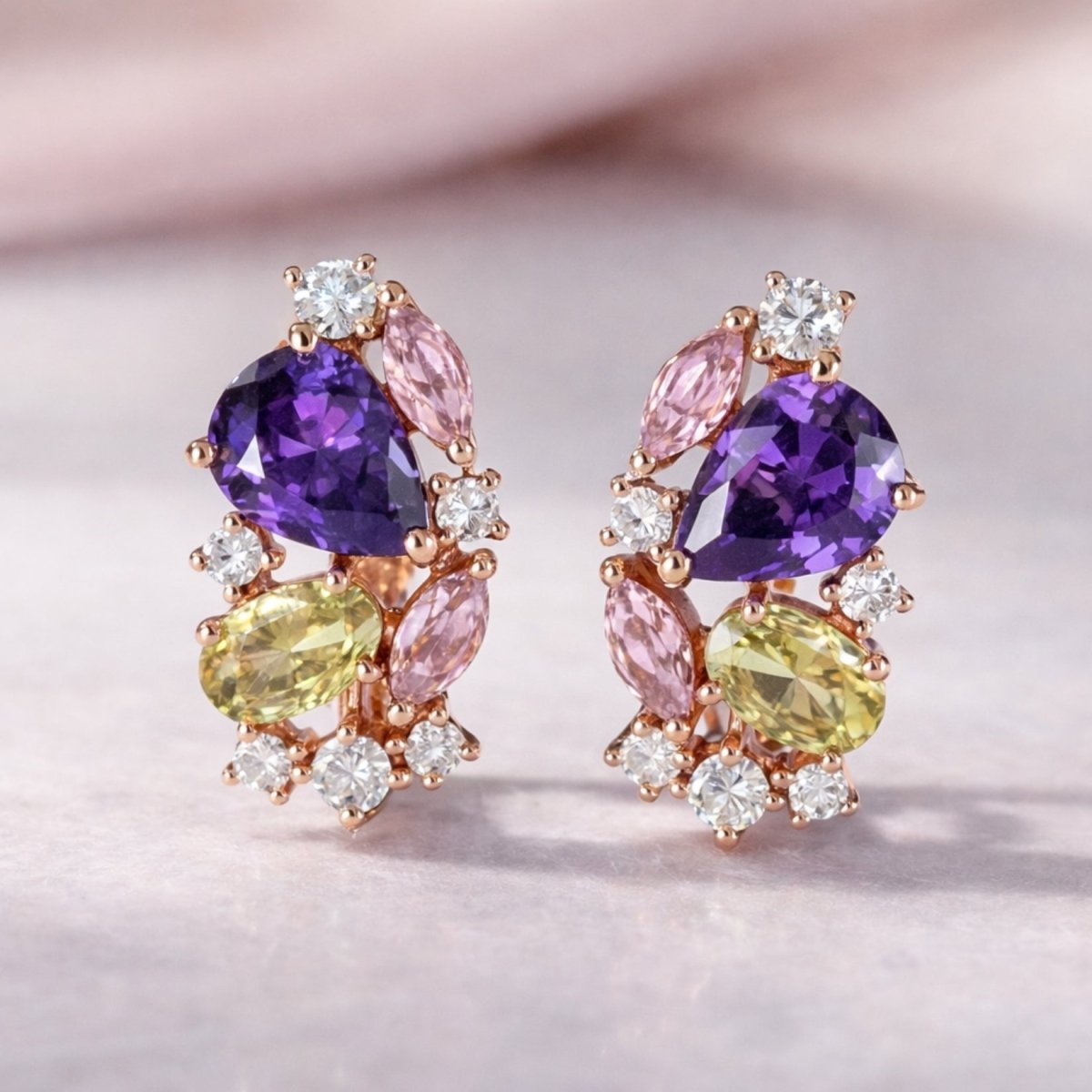 A direct front-view photo of the Kouvr Vanya multi-gemstone cluster earrings on a soft pink surface, highlighting the arrangement of the colorful stones.